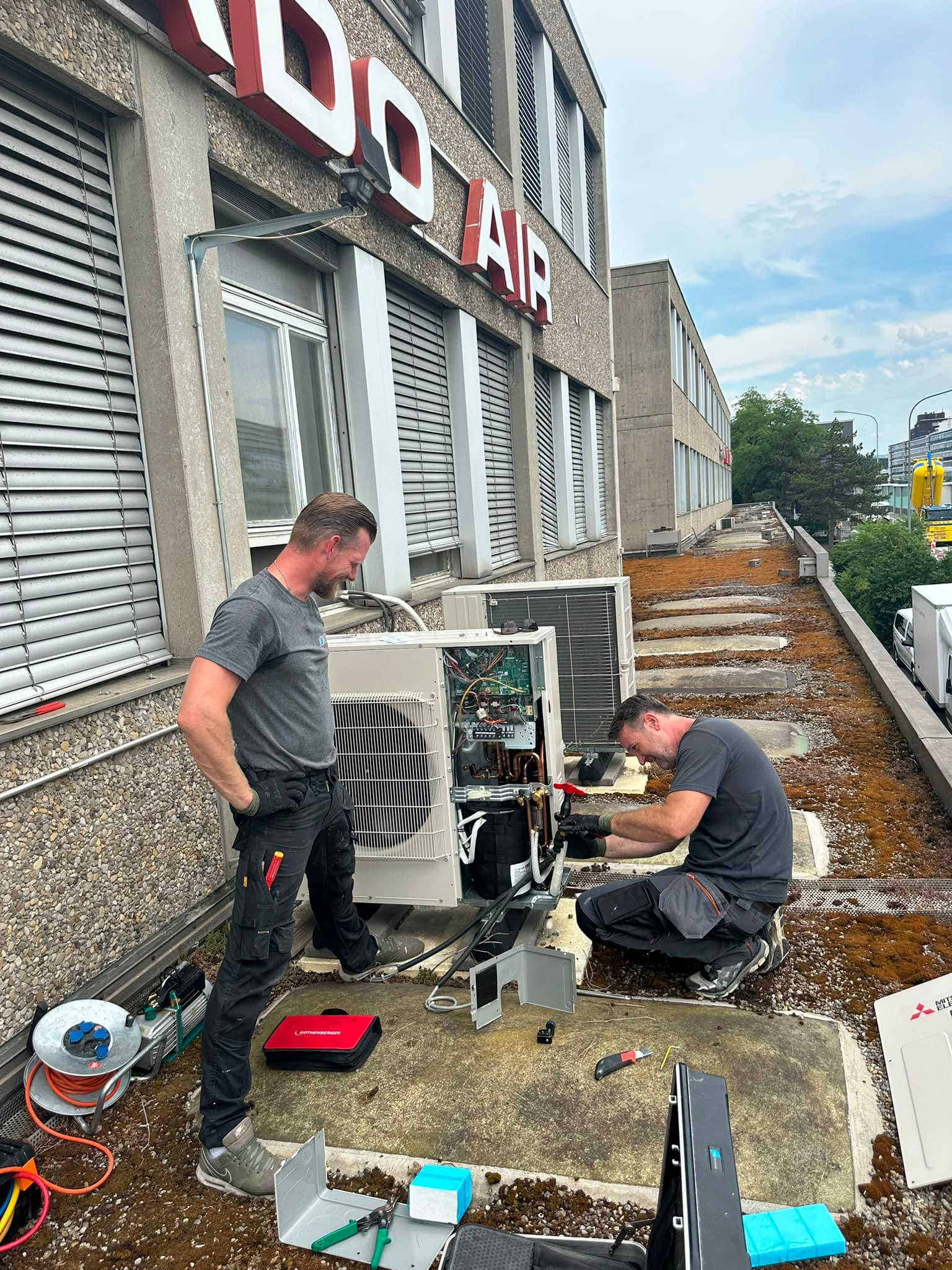 Zwei ICK-Techniker warten ein Aussengerät auf einem Firmendach, Kanton Zürich